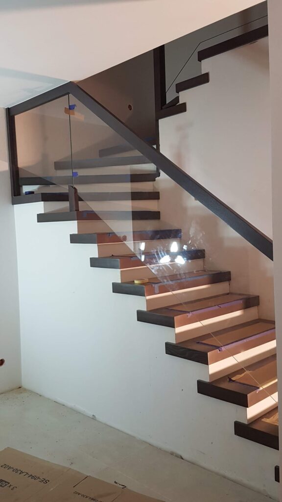 jasne podświetlane schody z czarną poręczą i szklaną ścianką