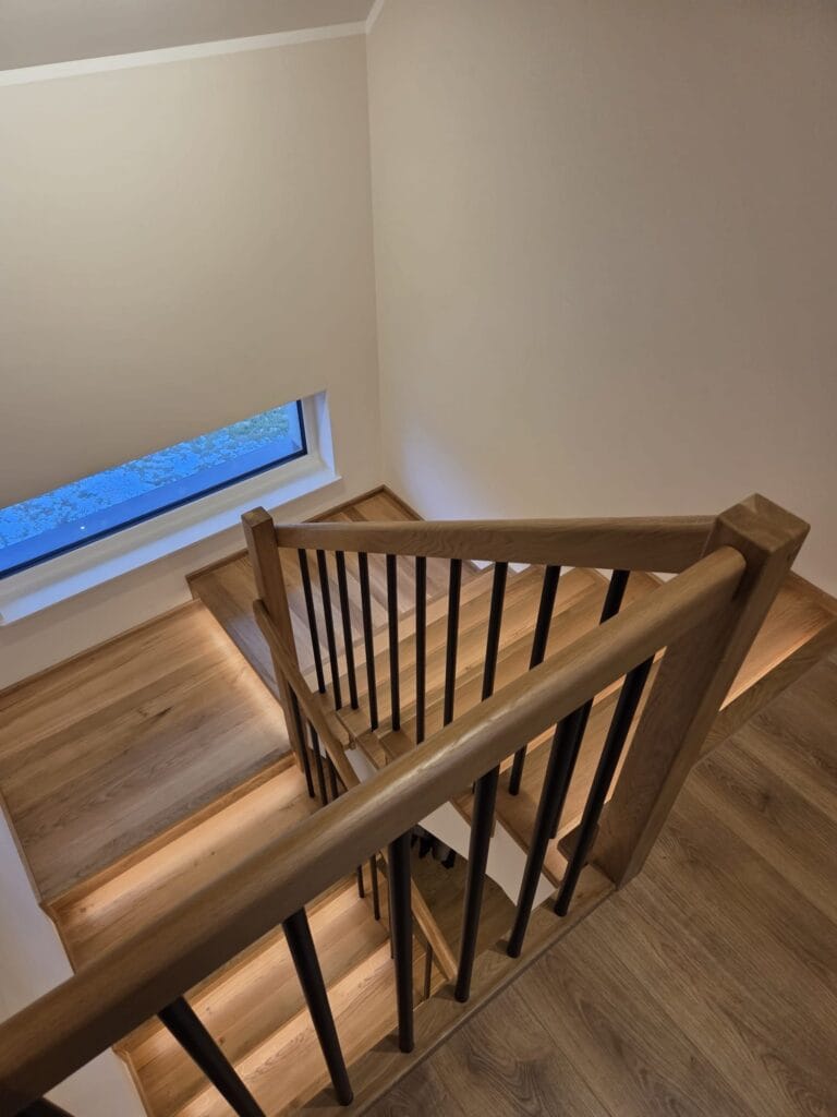 Drewniane schody z oświetleniem LED i czarną balustradą